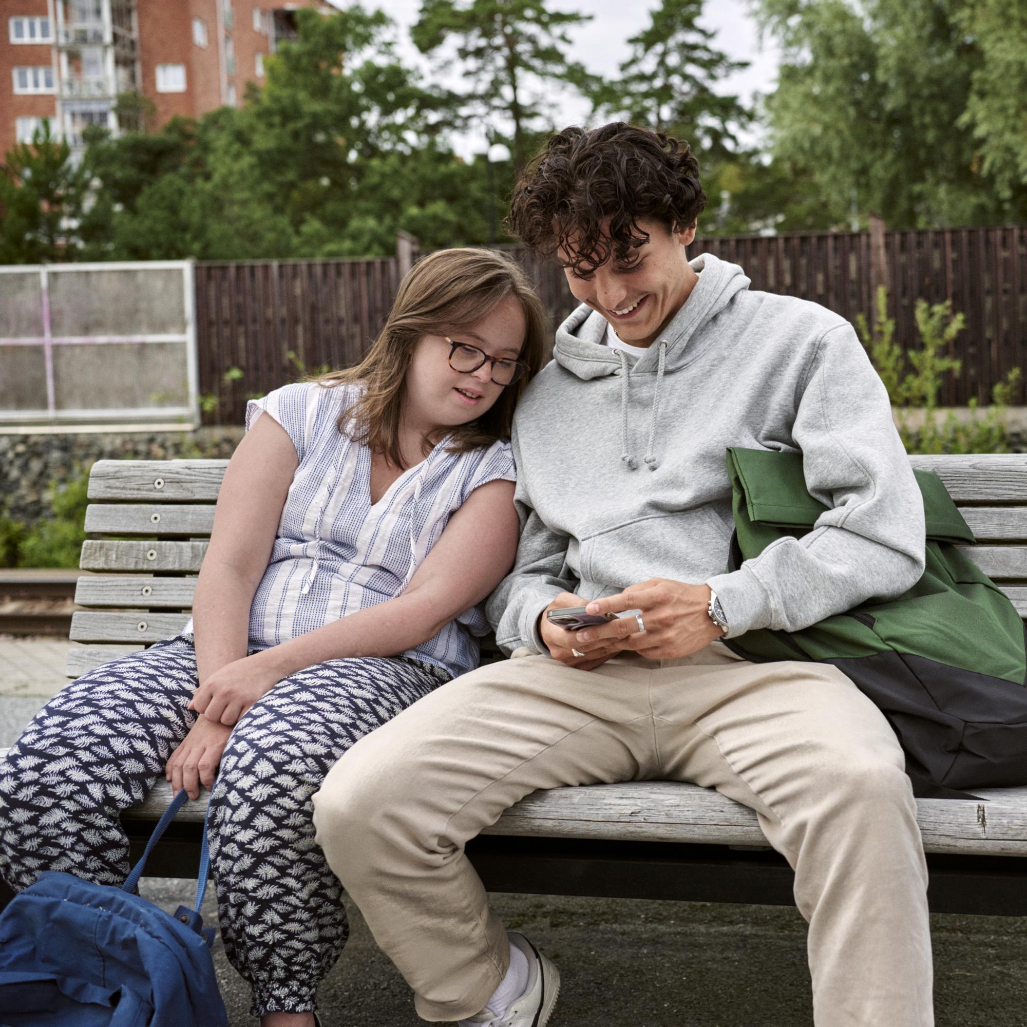 Två unga personer sitter utomhus med kartor och mobiler och planerar en resa