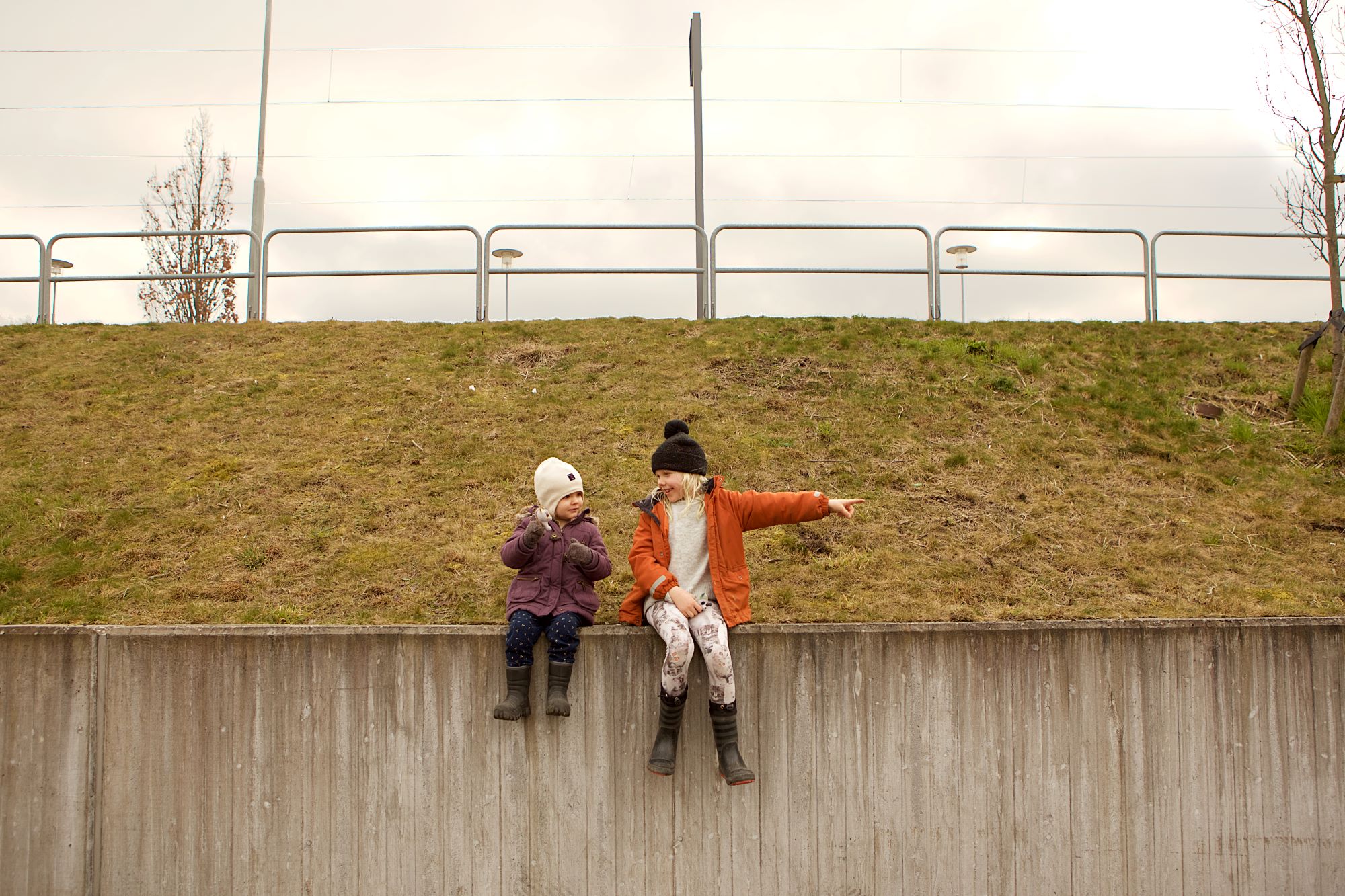 Två barn sitter på mur på hösten